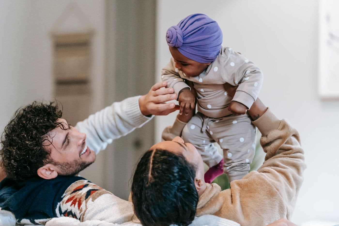 Parents at home lifting their baby in the air, laughing together